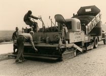 847897 Afbeelding van een asfalteermachine van de firma Strijland (Uithoorn) achter een vrachtwagen, tijdens het ...